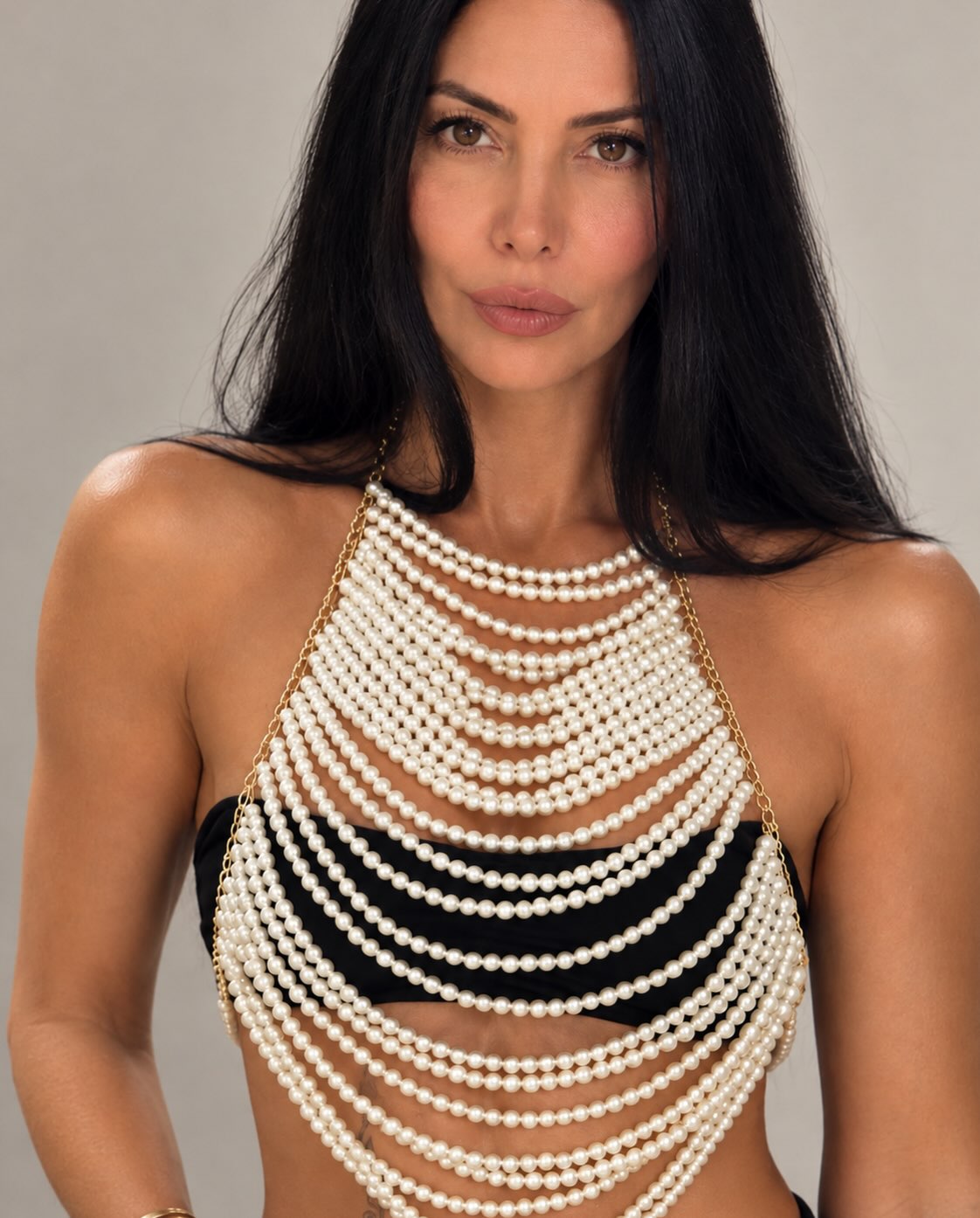 Close-up of layered white pearl body jewelry styled over a black top for LUMI.
