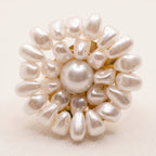 Macro photograph of the handmade Alba Pearl Bloom Ring by LUMI, highlighting its central white pearl surrounded by layered teardrop-shaped pearl beads arranged in a floral design.