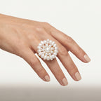 Hand wearing the handmade Alba Pearl Bloom Ring by LUMI, featuring a sculptural white pearl flower design with a central round pearl and gold-tone metal detailing.