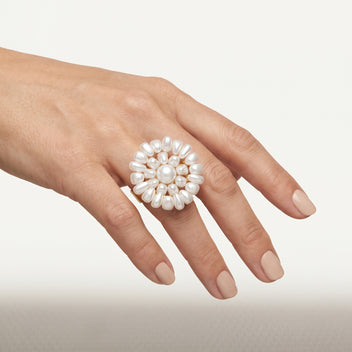 Hand wearing the handmade Alba Pearl Bloom Ring by LUMI, featuring a sculptural white pearl flower design with a central round pearl and gold-tone metal detailing.