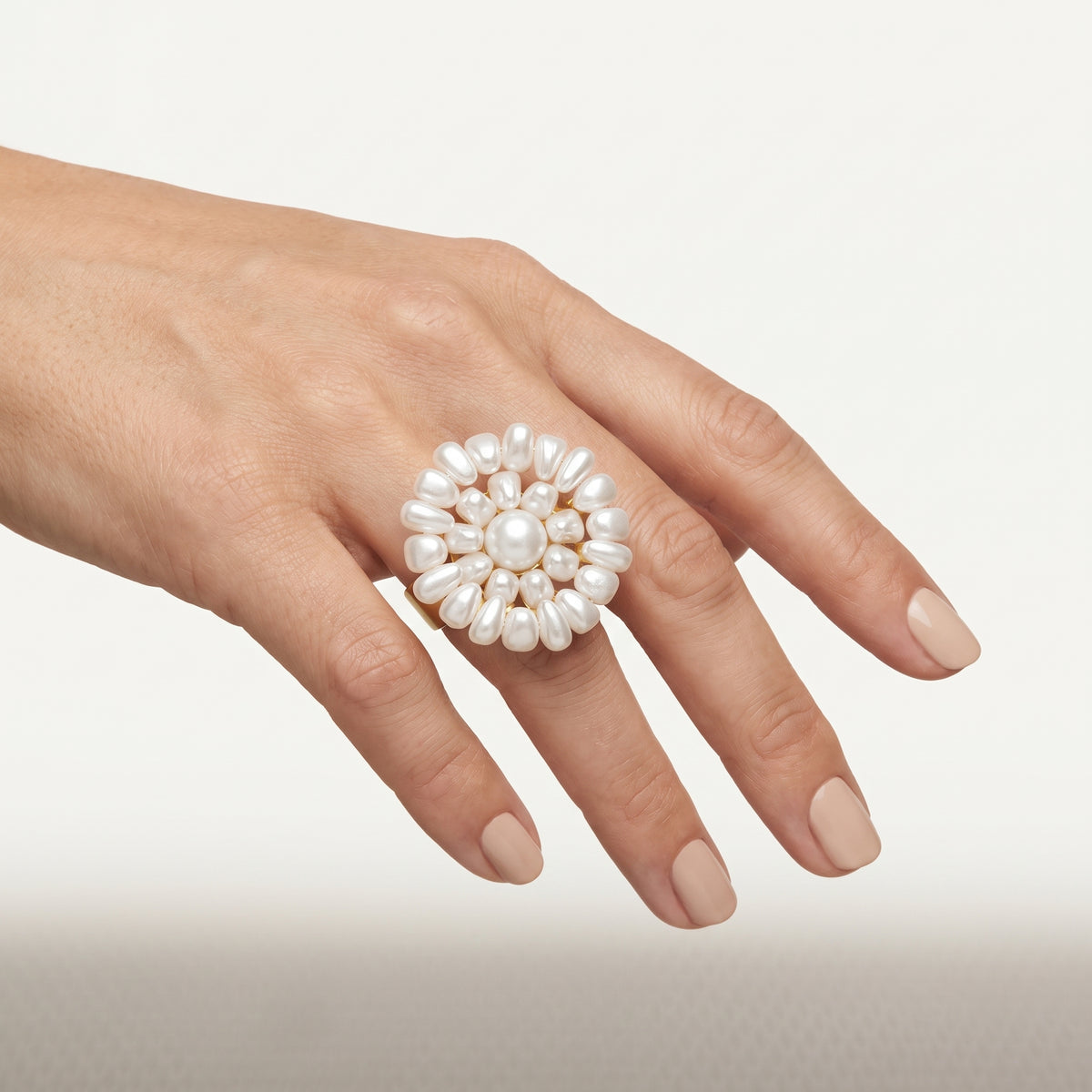 Hand wearing the handmade Alba Pearl Bloom Ring by LUMI, featuring a sculptural white pearl flower design with a central round pearl and gold-tone metal detailing.