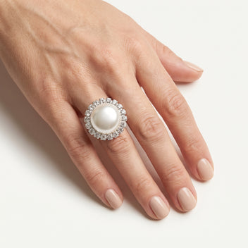 Close-up of a hand wearing LUMI's handmade Celestia Pearl Halo Ring – White, showcasing its luminous white pearl centerpiece, sparkling crystal halo and silver-tone setting.