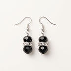 Pair of Éclipse crystal drop earrings by LUMI, featuring faceted black glass crystal beads, clear sparkling glass crystal spacer accents and silver-tone fishhook ear wires on a white background.