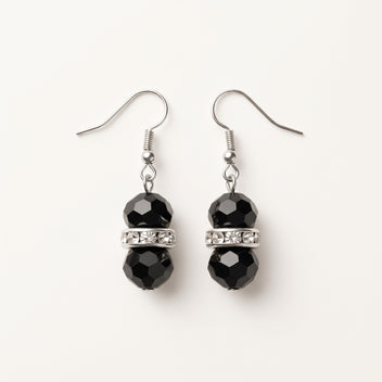 Pair of Éclipse crystal drop earrings by LUMI, featuring faceted black glass crystal beads, clear sparkling glass crystal spacer accents and silver-tone fishhook ear wires on a white background.