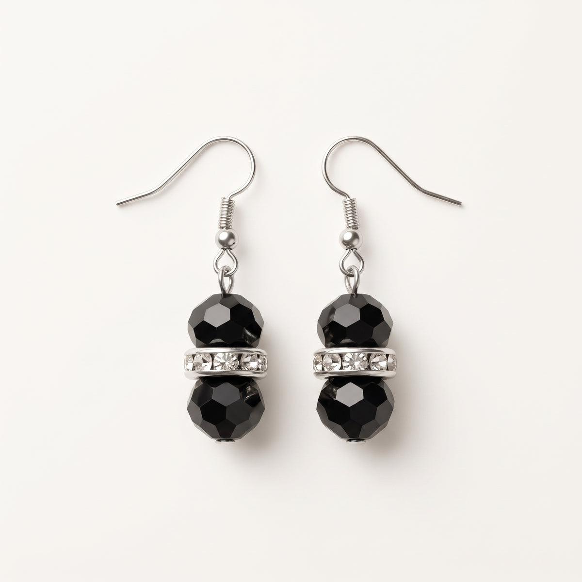 Pair of Éclipse crystal drop earrings by LUMI, featuring faceted black glass crystal beads, clear sparkling glass crystal spacer accents and silver-tone fishhook ear wires on a white background.
