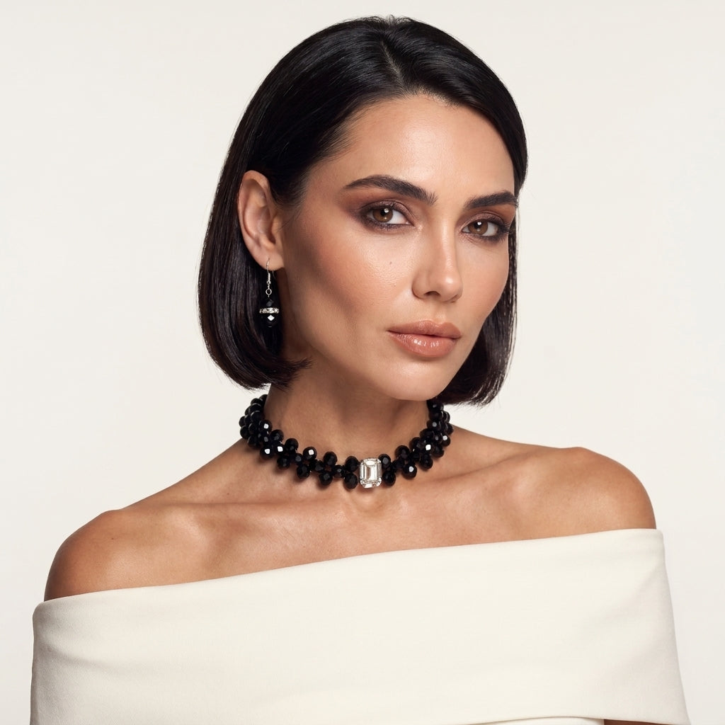 Fashion model wearing LUMI's Éclipse Crystal Choker Jewelry Set – Noir, featuring a sculptural black crystal necklace with a clear rectangular centerpiece and matching black crystal earrings, styled with an ivory off-shoulder outfit.