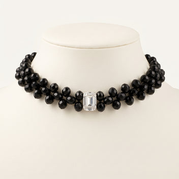 Close-up of the handmade Éclipse Crystal Choker Necklace by LUMI, highlighting clustered faceted black glass crystal beads and a rectangular clear glass crystal centerpiece against an ivory jewelry display.