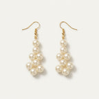 Close-up of the matching Elara ivory pearl drop earrings by LUMI, featuring clustered pearlescent beads and gold-tone hook fastenings against a light background.