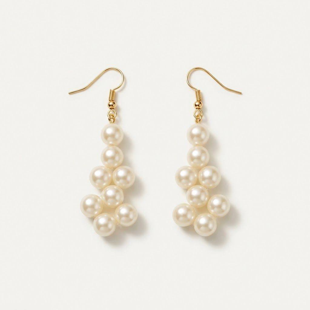 Close-up of the matching Elara ivory pearl drop earrings by LUMI, featuring clustered pearlescent beads and gold-tone hook fastenings against a light background.