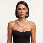 Model wearing the handmade Elara Ivory Pearl Jewelry Set by LUMI, featuring a V-shaped pearl necklace and matching drop earrings styled with a black strapless corset.