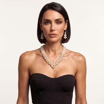 Model wearing the handmade Elara Ivory Pearl Jewelry Set by LUMI, featuring a V-shaped pearl necklace and matching drop earrings styled with a black strapless corset.