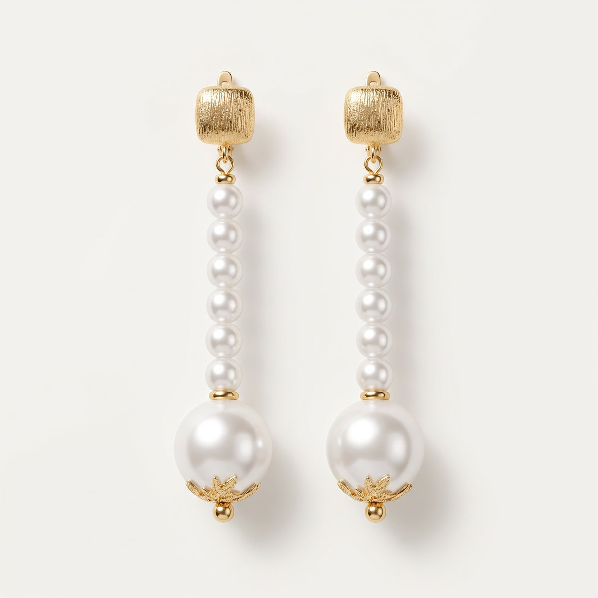 Pair of Éloise Pearl Drop Earrings by LUMI, featuring small white pearl beads arranged in elongated drops, larger pearl accents, textured gold-tone tops and decorative gold-tone caps.