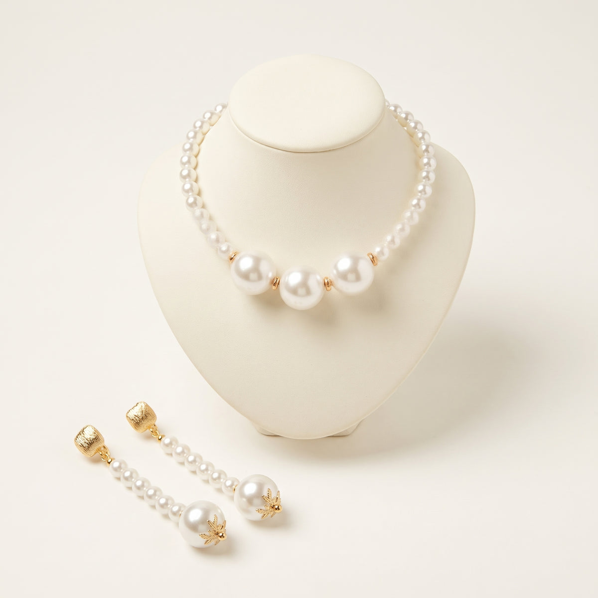 Handmade Éloise Pearl Trio Jewelry Set – White by LUMI, featuring a white pearl necklace with three large central pearls and matching long pearl drop earrings with gold-tone details on an ivory display.
