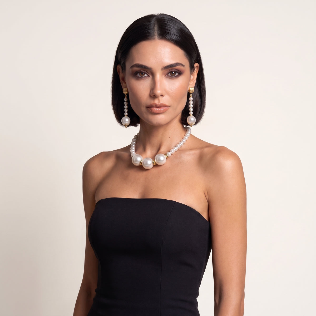 Fashion model wearing LUMI's Éloise Pearl Trio Jewelry Set – White, featuring a white pearl necklace with three prominent central pearls and matching long pearl drop earrings, styled with a black strapless dress.