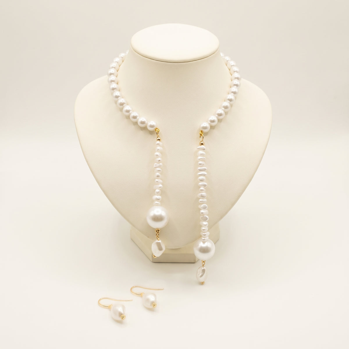 Handmade Joyelle Pearl Drop Jewelry Set – White by LUMI, featuring an asymmetrical white pearl necklace with two cascading strands and matching pearl drop earrings, displayed on an ivory jewelry bust.