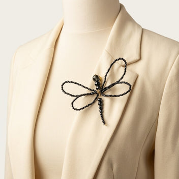 Close-up of the handmade Libellule Navy Crystal Dragonfly Brooch by LUMI pinned to an ivory blazer lapel, showcasing its four crystal-beaded wings and elegant gold-tone detailing.