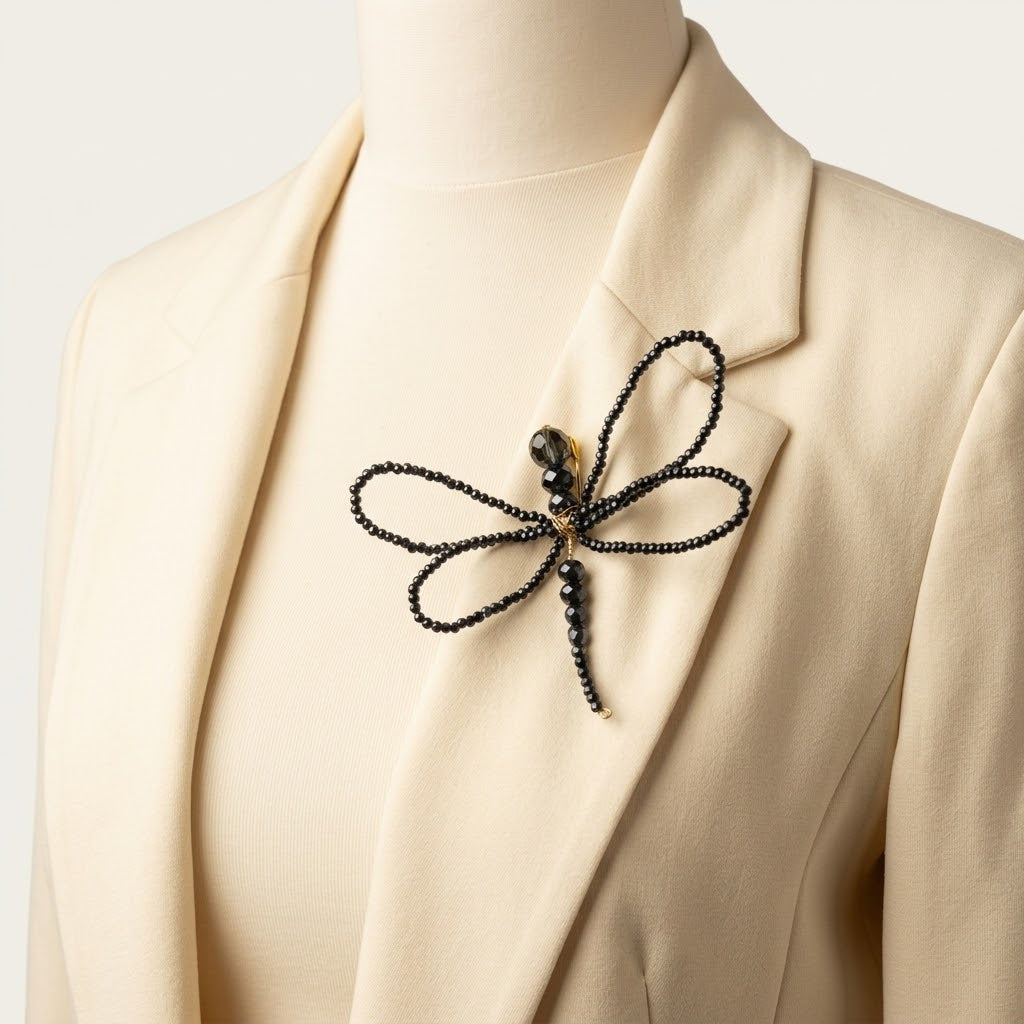 Close-up of the handmade Libellule Navy Crystal Dragonfly Brooch by LUMI pinned to an ivory blazer lapel, showcasing its four crystal-beaded wings and elegant gold-tone detailing.
