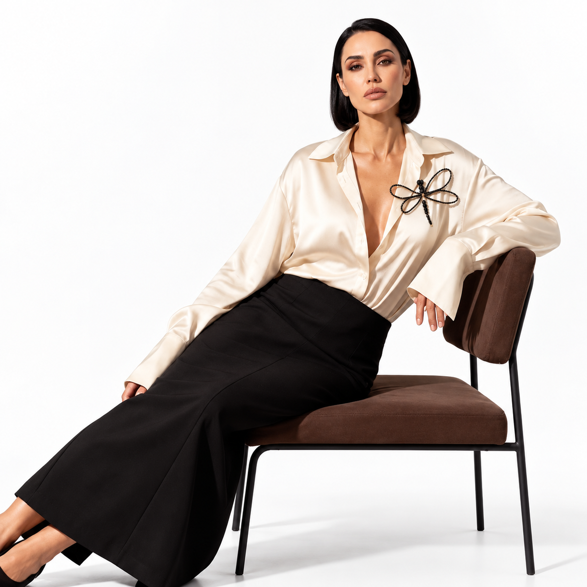 Fashion model wearing the handmade Libellule Navy Crystal Dragonfly Brooch by LUMI on an ivory blouse, styled with black trousers against a warm brown studio background.