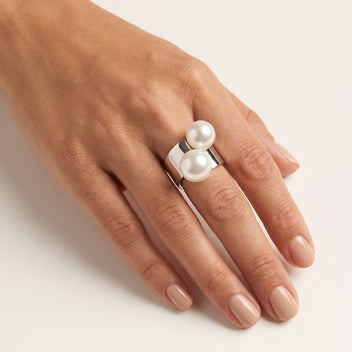 Close-up of a hand wearing the handmade Solène Double Pearl Ring by LUMI, showcasing two luminous white pearls on a wide silver-tone metal band.