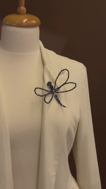 Luxury editorial video featuring LUMI's handmade black crystal dragonfly brooch on an ivory couture blazer, highlighting its intricate beaded wings and shimmering details.
