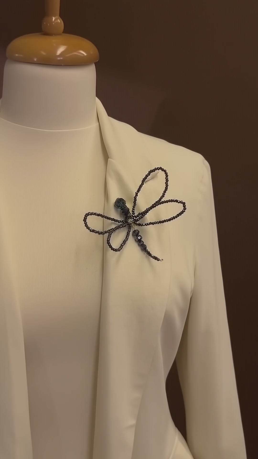 Luxury editorial video featuring LUMI's handmade black crystal dragonfly brooch on an ivory couture blazer, highlighting its intricate beaded wings and shimmering details.