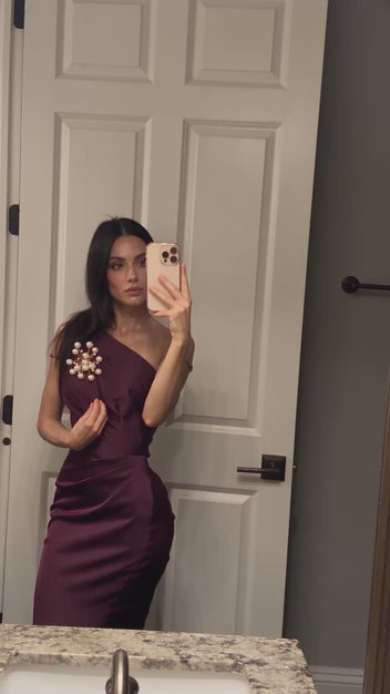 Model wearing the handmade Astra Pearl Burst Brooch by LUMI on a burgundy one-shoulder dress, showing the sculptural white pearl and gold-tone design in motion.