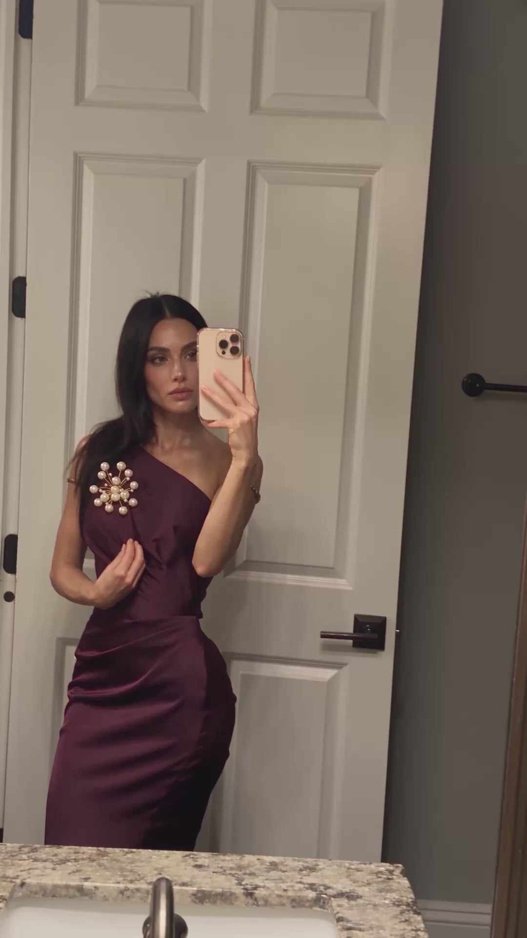 Model wearing the handmade Astra Pearl Burst Brooch by LUMI on a burgundy one-shoulder dress, showing the sculptural white pearl and gold-tone design in motion.