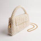 Angled view of The Nacre Bag showing the pearl construction, gold-tone chain strap and LUMI charm.