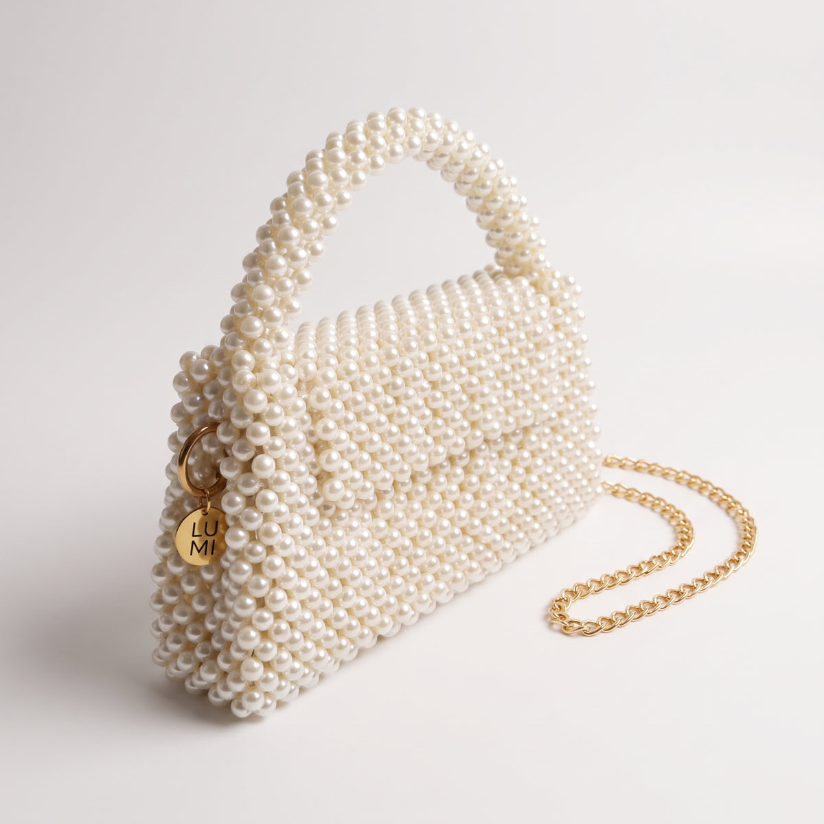 Angled view of The Nacre Bag showing the pearl construction, gold-tone chain strap and LUMI charm.