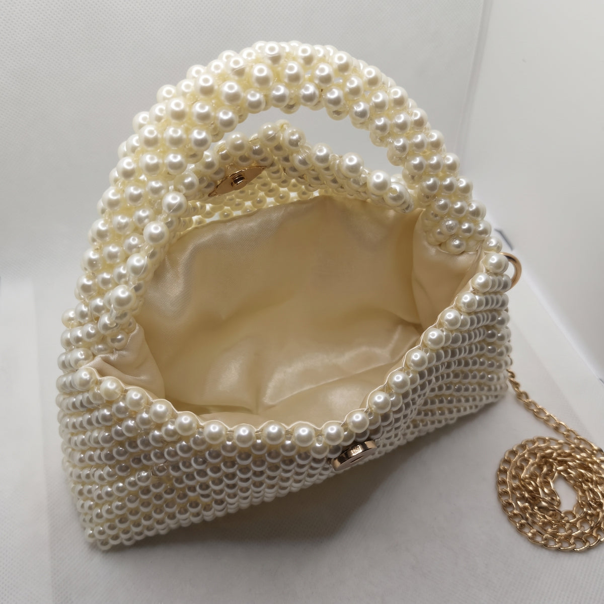 Open view of The Nacre Bag showing its soft satin interior lining and pearl-covered structure.