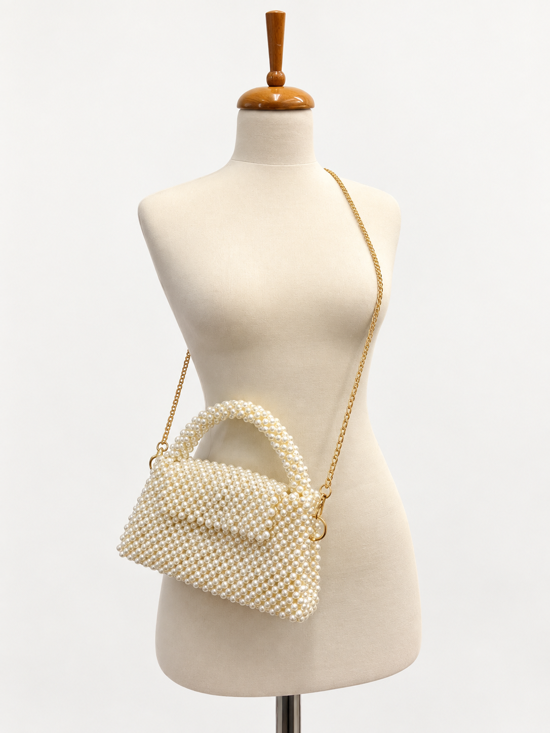The Nacre pearl handbag displayed with its gold-tone shoulder chain on an ivory mannequin.